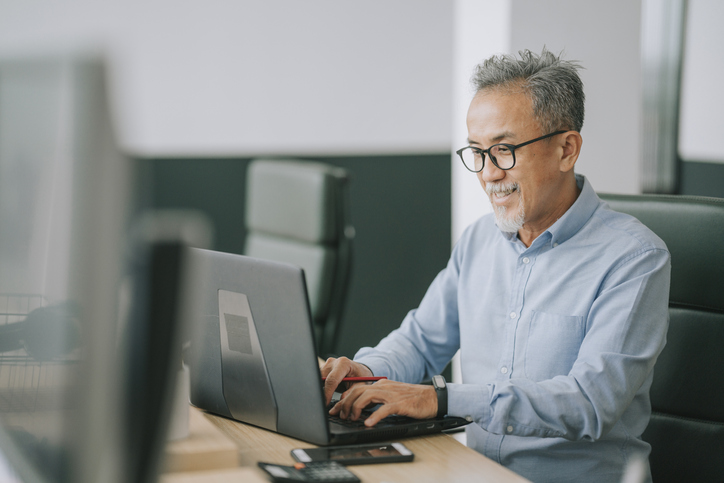 Boost Productivity with Fiber Internet Older Asian Man sitting at a work desk with a laptop