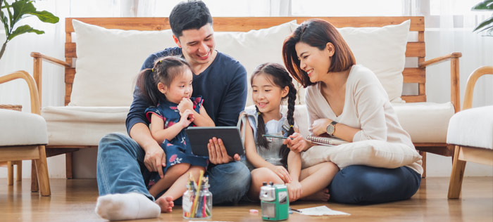 smiling Asian family of four sitting on the living room floor looking at a tablet
